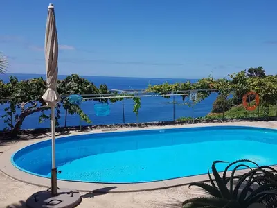 a swimming pool with an umbrella and the ocean at Quinta Golfinho - Casa Nenufar in Arco da Calheta