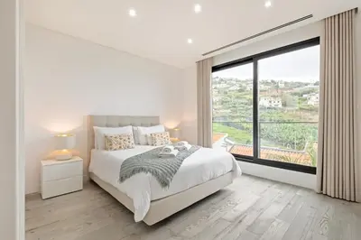 a white bedroom with a bed and a large window at Casa Susan in Ribeira Brava