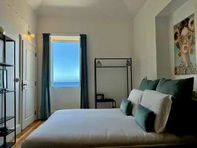 a white building with black shuttered windows and the ocean at Espada Preta Apartments in Câmara de Lobos