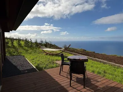 a table and chairs on a deck with the ocean at Sunset Eco Shelter 1 in Ponta do Pargo