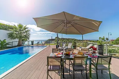 a dining table with an umbrella next to a swimming pool at Villa Sol e Mar Dio by Villa Plus in Caniço
