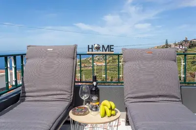 a balcony with two beds and a table with a glass of wine and bananas at Estrela House I Calheta Madeira in Calheta