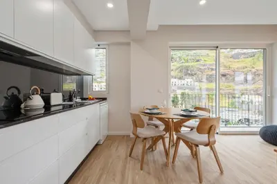 a kitchen with a table and chairs and a kitchen with white cabinets at Modern Flat Just Steps From Shore in Ponta do Sol