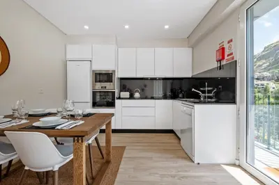 a kitchen with a wooden table and white cabinets at Modern Apartment Steps From Beach in Ponta do Sol