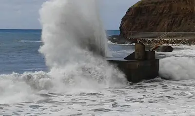 a wave is spraying into the water on a beach at Penthouse Marina Sol in Madalena do Mar