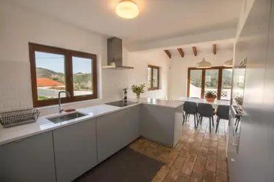 a kitchen with white cabinets and a table with chairs at Cabasina Bordeira in Bordeira
