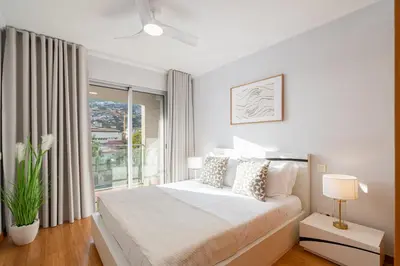 a white bedroom with a bed and a large window at Anchored in Carmo by Homie in Câmara de Lobos