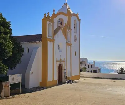 a church with a clock tower in front of the ocean at Vivenda Chagas in Luz