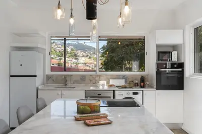 a kitchen with white cabinets and a large window at Casa da Anoneira House with Pool and Sea View in Funchal