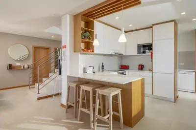 a kitchen with white cabinets and a counter with stools at OurMadeira - Casa Laranja in Prazeres