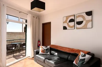 a living room with a black leather couch and a balcony at Solful at the Nomads Village Ponta do Sol in Ponta do Sol
