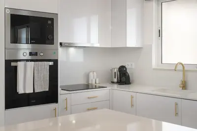 a kitchen with white cabinets and a black appliance at Central Park Caniço Central Modern & Cozy in Santa Cruz