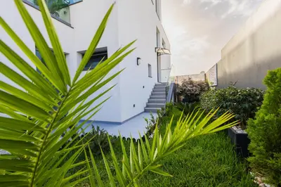 a white house with green plants in the yard at VILLA HELENA Pearl Apartment in Caniço