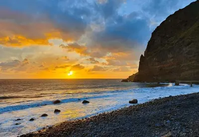 a sunset on a beach with a rocky shore at Casa Rodrigues in Madalena do Mar