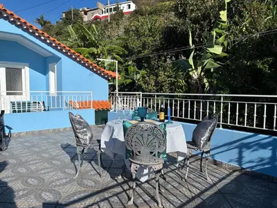 a table and chairs in front of a blue house at Sea & Mountain View Home in Machico in Machico