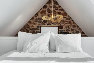 a bed with white pillows and a triangular ceiling at Romantic Retreat by Slice of Heaven in Jardim do Mar