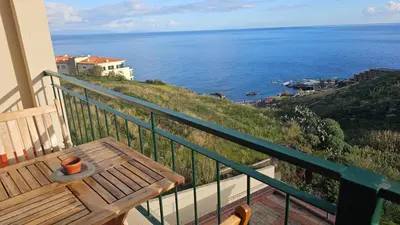 a balcony with a wooden bench and the ocean at Reis Magos View in Caniço