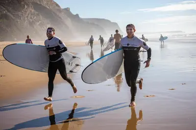 two men running on the beach with their surfboards at Ocean View Apartment near Arrifana Beach with Parking in Aljezur