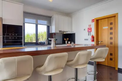 a kitchen with a bar with white bar stools at Oasis do Sol, a Home in Madeira in Ponta do Sol