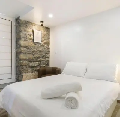 a bedroom with a large white bed with a stone wall at Casa Dos Avós - Sea View Studio in São Vicente