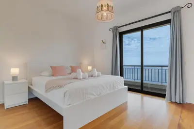 a white bedroom with a bed and a large window at Bay Bliss - Ocean & City View by AH in São Gonçalo