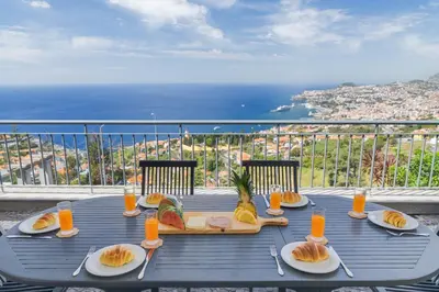 a table with plates of food on a balcony at Bay Bliss - Ocean & City View by AH in São Gonçalo