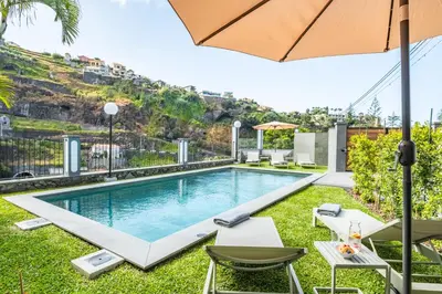 an outdoor pool with chairs and an umbrella at Central Apartment Steps From Beach in Ponta do Sol