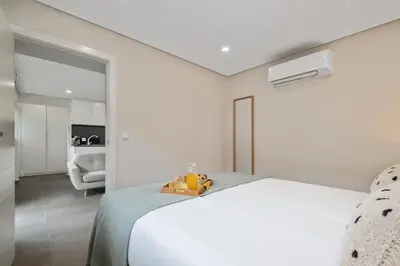 a white bedroom with a bed and a living room at Central Apartment Steps From Beach in Ponta do Sol