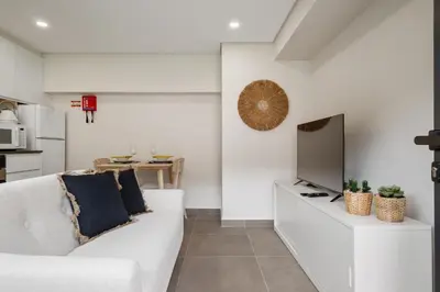 a living room with a white couch and a tv at Central Apartment Steps From Beach in Ponta do Sol