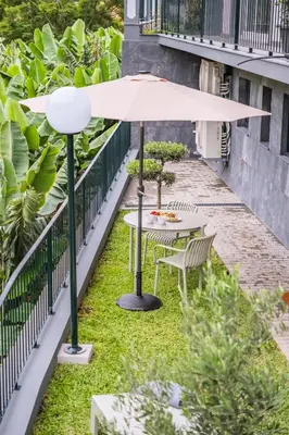 a table and chairs under an umbrella on the grass at Central Apartment Steps From Beach in Ponta do Sol
