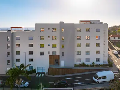 a white building with a white van parked in a parking lot at Atlantic Pearl Pool & Ocean View One Bedroom Apartment in Câmara de Lobos