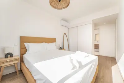 a white bedroom with a large bed and a clock at Atlantic Pearl Pool & Ocean View One Bedroom Apartment in Câmara de Lobos