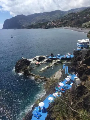 a beach with blue and white umbrellas and the water at Casa do Cavacas in Funchal