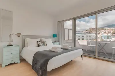 a white bedroom with a bed and a large window at Arriaga apartment in Funchal