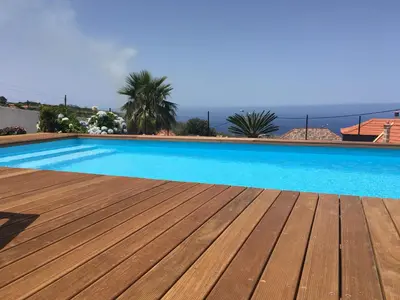 a large swimming pool with a wooden deck and the ocean at Casa das Marias in Ponta do Pargo