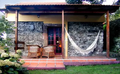 a porch with two wicker chairs and a stone wall at Pestana Quinta do Arco Nature & Rose Garden Hotel in Arco de São Jorge