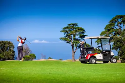 a man hitting a golf ball with a golf cart at Palheiro Village Resort in Funchal