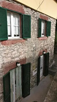 a stone building with green shutters and a door at Casa da Guida in Paul do Mar