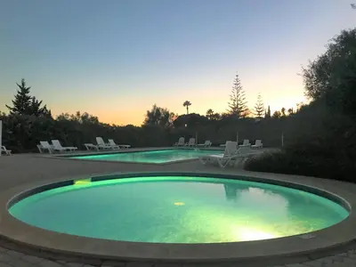 two swimming pools with chairs and a sunset in the background at Casas do Ramalhete in Luz