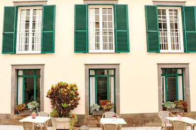 a building with green windows and tables and chairs at Amparo in Machico