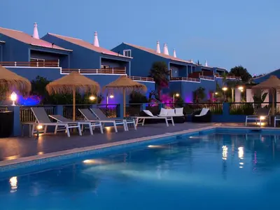 a hotel swimming pool with chairs and umbrellas at night at Aldeia Azul Resort in Lagos