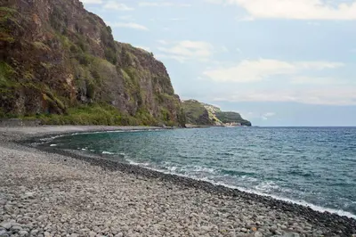 a rocky beach next to the ocean with a mountain at Casa do Lugar de Baixo in Ponta do Sol
