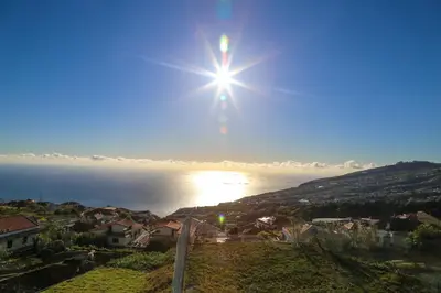 a sun shining over the water in a town at A&M House in Arco da Calheta