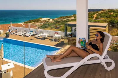 a woman sitting in a chair reading a book by a pool at Mareta Beach House - Boutique Residence in Sagres
