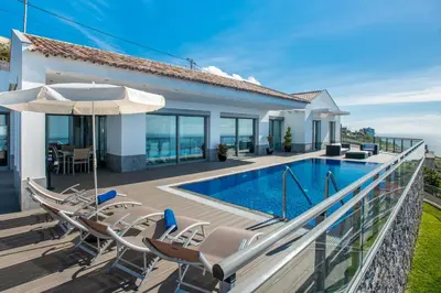 a house with a swimming pool with chairs and an umbrella at Villa São Lourenço in Fajã da Ovelha