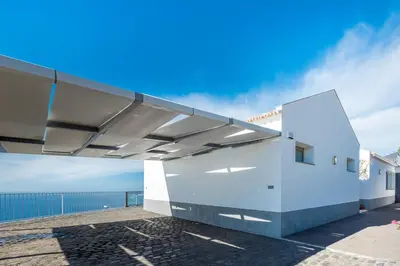 a white building with a roof with the ocean in the background at Villa São Lourenço in Fajã da Ovelha