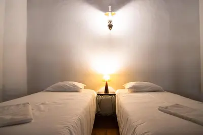 two beds in a room with a light on the wall at Carrapateiramar Guest House in Carrapateira