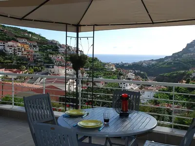 a table with two chairs and an umbrella on a balcony at Quinta da Torre in Câmara de Lobos