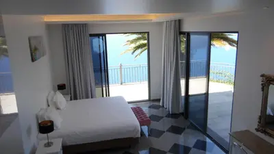 a bedroom with a bed and a balcony with the ocean at Ocean Cliff in Ponta do Sol