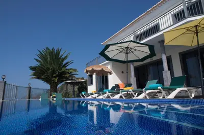 a pool with chairs and umbrellas next to a house at Ocean Cliff in Ponta do Sol